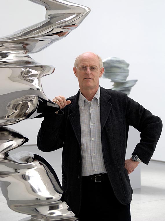 Illustration for: Tony Cragg in front of another stainless steel sculpture. © VG Bild-Kunst, Bonn 2025